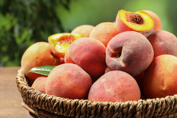 Cut and whole fresh ripe peaches in basket on wooden table against blurred background, closeup. Space for text