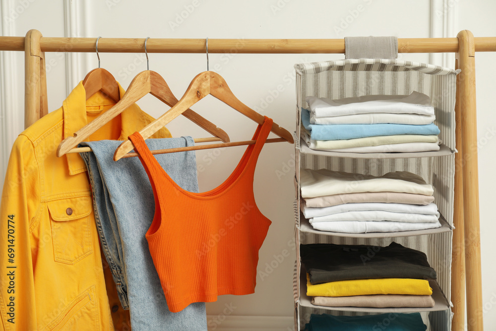 Sticker Wardrobe organization. Rack with different stylish clothes near white wall