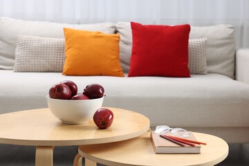 Red apples with book on nesting tables and comfortable sofa in living room. Interior design