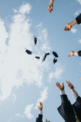 A group of happy students celebrating graduation in a park, throwing caps in the air, symbolizing...
