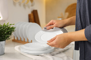 Woman wiping plate with towel in kitchen, closeup