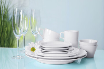 Set of clean dishware and flower on light blue table