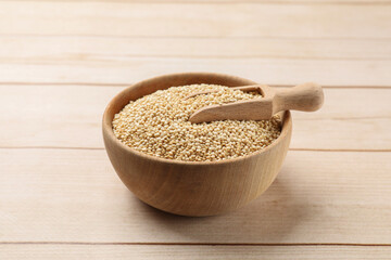 Bowl and scoop with raw quinoa on wooden table, closeup