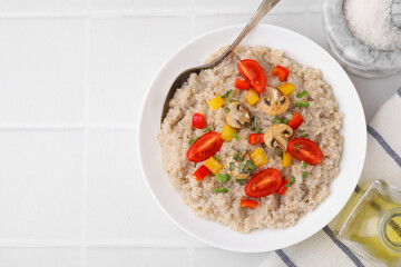 Delicious barley porridge with vegetables and microgreens in bowl served on white tiled table, flat lay. Space for text