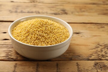 Millet groats in bowl on wooden table, space for text