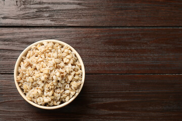 Delicious pearl barley in bowl on wooden table, top view. Space for text