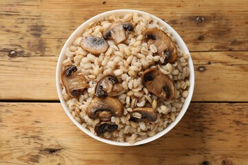 Delicious pearl barley with mushrooms in bowl on wooden table, top view