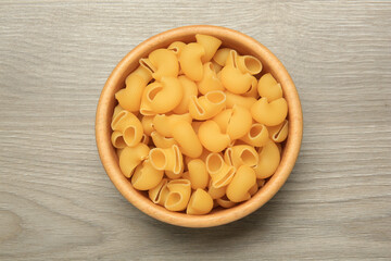 Raw macaroni pasta in bowl on light grey wooden table, top view