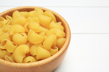 Raw macaroni pasta in bowl on white wooden table, closeup