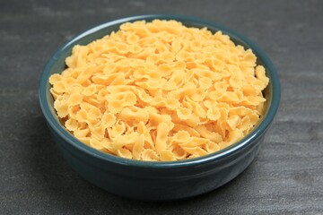 Raw farfalline pasta in bowl on grey table, closeup