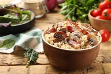 Tasty quinoa porridge with fried bacon and mushrooms in bowl on wooden table, closeup. Space for text