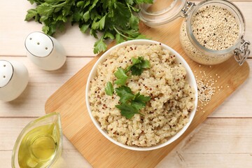 Tasty quinoa porridge with parsley in bowl and seeds on light wooden table, flat lay