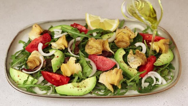 Warm salad with rapan (snails), tomatoes, avocado, onions, leafy vegetables, lemon and olive oil. Traditional salad with seafood. A woman pours oil on a salad. Close-up, selective focus.