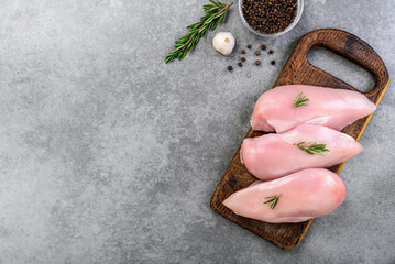 Raw chicken breast with spices on wooden board on gray background.
