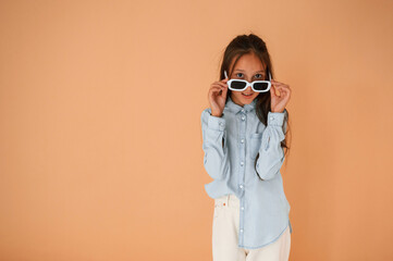 In stylish glasses. Cute young girl is in the studio against background