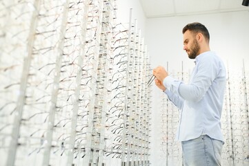 Naklejka na ściany i meble Young man choosing spectacles at optic shop