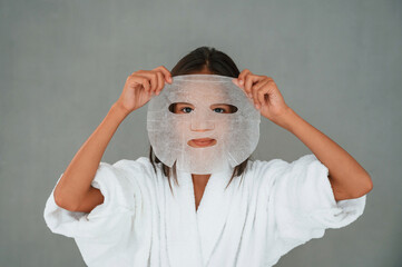 Against grey background. Holding mask for the face. Conception of beauty and self care. Young girl...