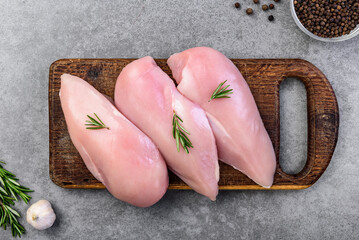 Raw chicken breast with spices on wooden board on gray background.