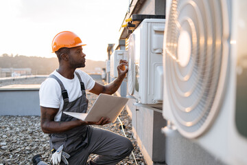 Responsible african american worker repairing device for cooling premises on rooftop with portable...