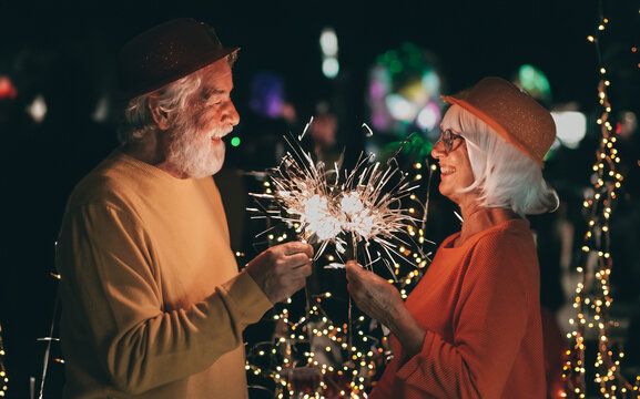 Celebrate event new year for couple of nice senior people sparkling lights - cheerful elderly caucasian man and woman having party by night. Happiness lifestyle for mature retired people