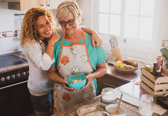 Mother and daughter in the home kitchen smiling and enjoying prepare meal together. Beautiful curly...
