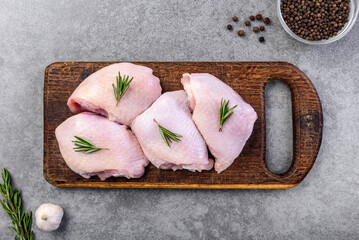 Raw chicken thighs on wooden board on gray background.