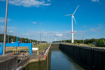 Naklejka premium This vibrant image features a maritime lock system on a clear day, set against a backdrop of sustainable energy with a towering wind turbine. The locks serve as critical infrastructure for managing