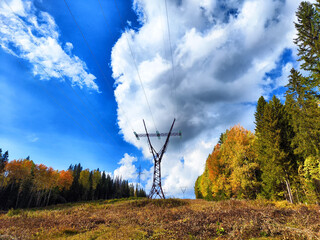 Power lines on a hill, hill or in the mountains against a blue sky with white clouds. Electric lines, towers, wires in the landscape