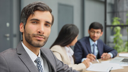 male boss against the background of her colleagues looks at the camera in a modern office