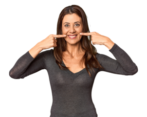 Elegant middle-aged Caucasian woman in studio setting smiles, pointing fingers at mouth.