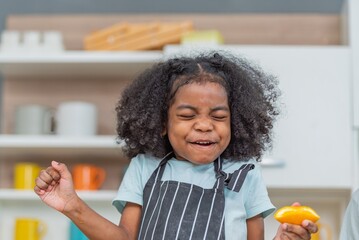 african afro hair black kid Cute taste oranges citrus sour flavour on ripe mouth in kitchen. candid...