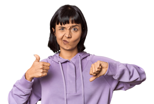 Young Hispanic woman with short black hair in studio showing thumbs up and thumbs down, difficult choose concept