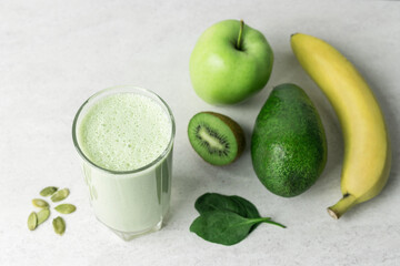 Green detox smoothie, blended vegetarian drink, protein milkshake in a glass from spinach, banana, apple, avocado, kiwi and seeds on a table, healthy eating concept