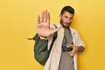 Young Hispanic travel photographer poses standing with outstretched hand showing stop sign,...
