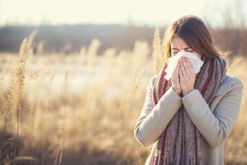 femme dans un champ en train d'éternuer à cause des allergies aux pollens - obrazy, fototapety, plakaty