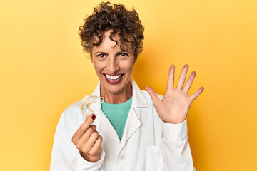 Doctor with invisible dental aligner on yellow smiling cheerful showing number five with fingers.