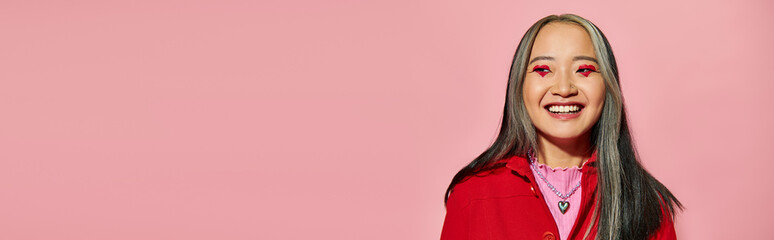 Valentines day banner, happy asian woman with heart shaped eye makeup posing on pink backdrop - Powered by Adobe
