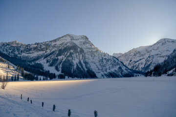 Last ray of sunshine on the Vilsalpsee. Shadow on the mountain slopes and frozen lake near Tannheim