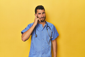 Young Hispanic male nurse Young Hispanic male nurse poses confidently pointing temple with finger, thinking, focused on a task.< mixto >