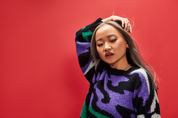 pretty young asian woman in sweater with animal print with heart shaped necklace posing on red