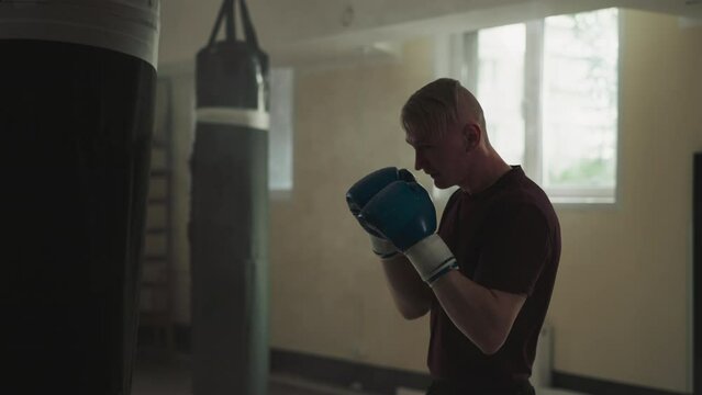 Boxer fights punching bag in empty sports club