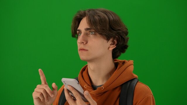 Portrait of person tourist isolated on chroma key green screen background. Close up shot young man holding smartphone looking at the departure board.