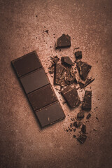 chocolate bar , for the manufacture of confectionery, broken, crumbled, on a brown background, top view,