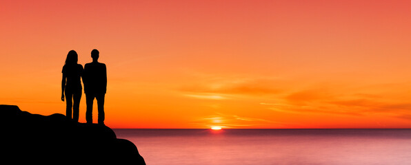 Sihouette eines Mannes und einer Frau auf einer Klippe bei Sonnenuntergang