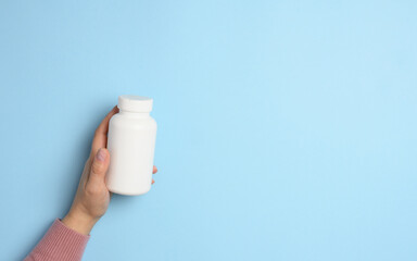 Two female hands holding a white plastic bottle for pills on a blue background