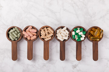 Vitamins and supplements. Variety of vitamin tablets in a wooden spoon on a texture background.Multivitamins with fresh and healthy fruits.Food supplements. Flat lay. Space for text.Copy space