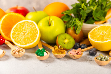Vitamins and supplements. Variety of vitamin tablets in a wooden spoon on a texture background.Multivitamins with fresh and healthy fruits.Food supplements. Flat lay. Space for text.Copy space
