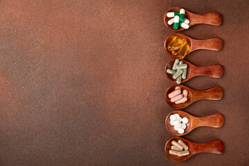 Vitamins and supplements. Variety of vitamin tablets in a wooden spoon on a texture background.Multivitamins with fresh and healthy fruits.Food supplements. Flat lay. Space for text.Copy space