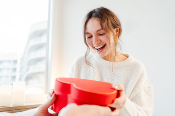 Excited beautiful woman holding gift box with. Happy romantic couple celebration birthday sitting at home. Dating, love, relationship, Valentines day concept