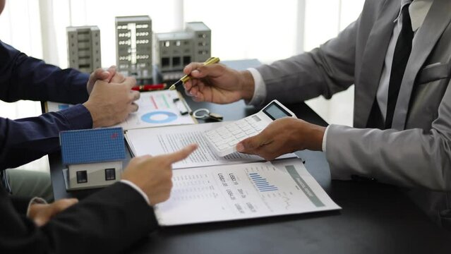 Businessman is negotiating a contract for the purchase and sale of a house. Real estate agent is offering a house for sale and a businessman signs an agreement document.